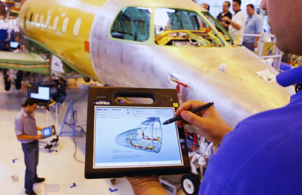 Engenheiro da Embraer analisa projeto digital de aeronave durante processo de fabricação em São José dos Campos.