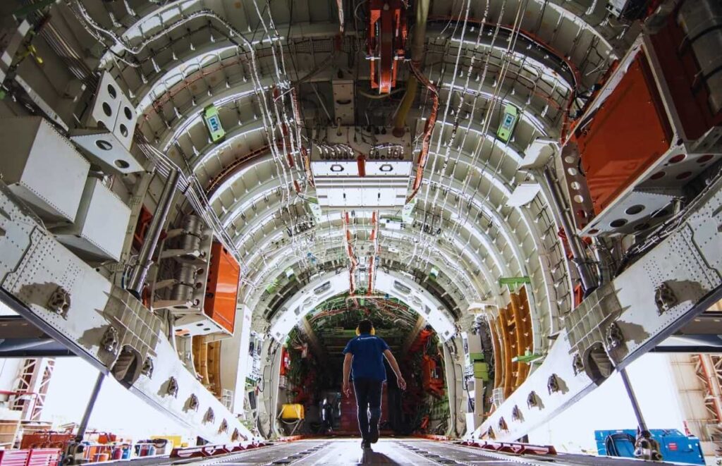 Engenheiro da Embraer caminha pelo interior da fuselagem de uma aeronave em fase de montagem, simbolizando o trabalho de alta complexidade da engenharia aeroespacial.